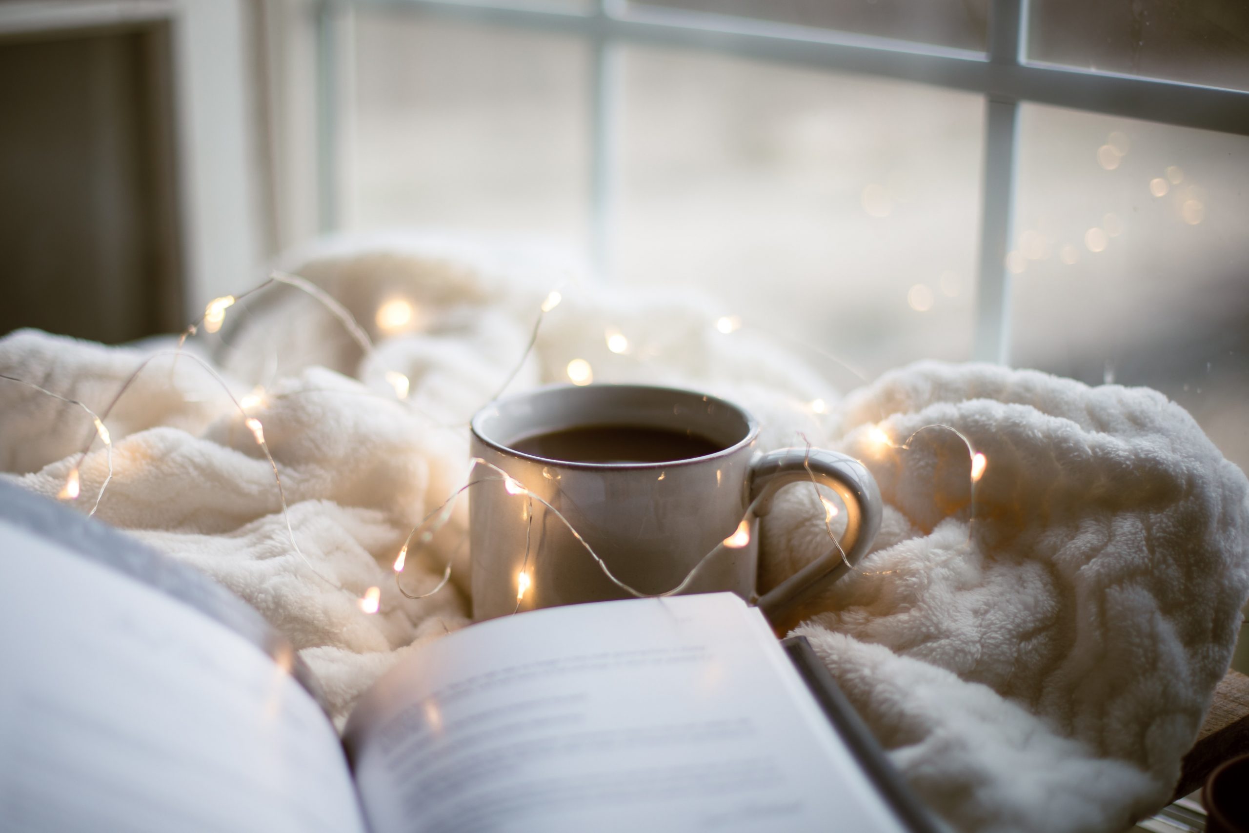 Open book and coffee cup on bed with blanket