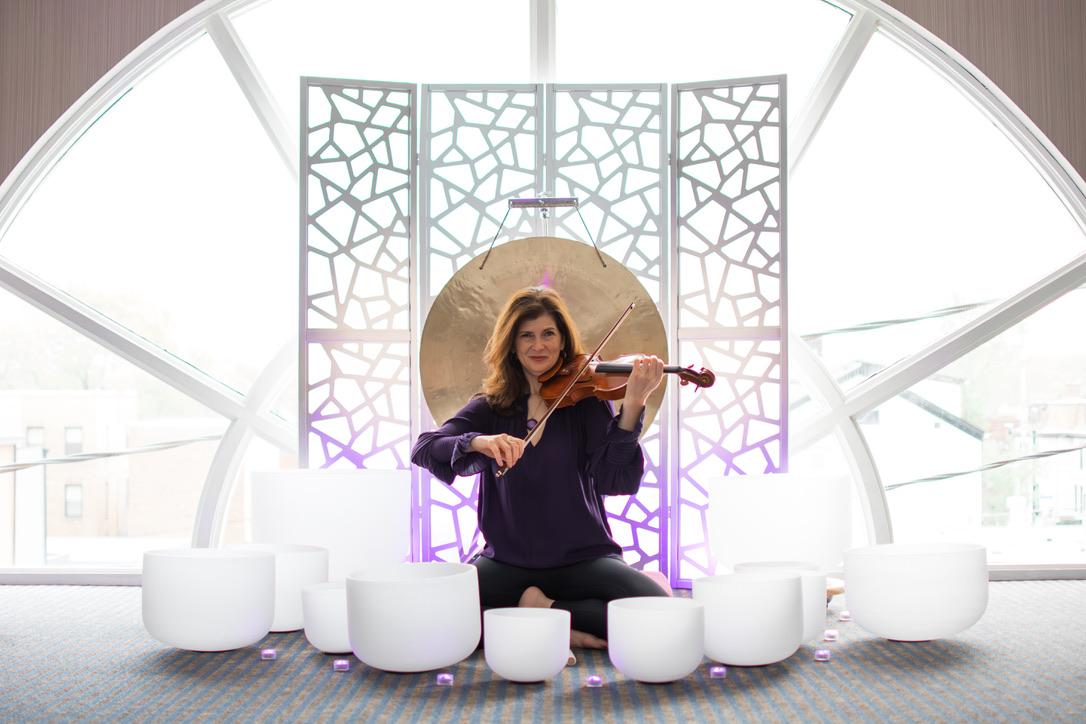 An individual playing the violin surrounded by various sizes of large white bowls.