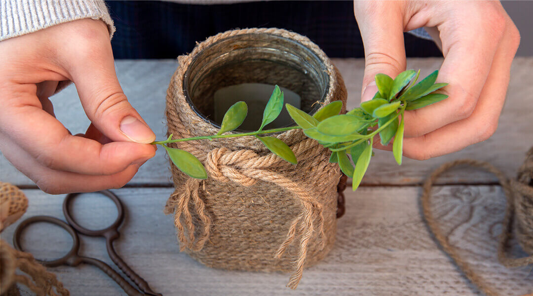 Hands holding a plastic plant over a jar wrapped in twine