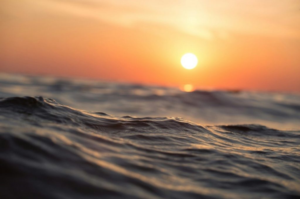 Photo of a bright orange sunset over choppy ocean waves.  